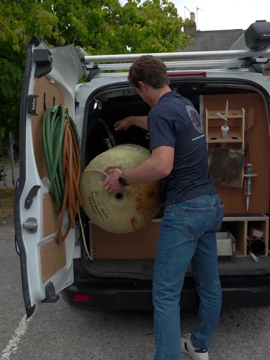 An engineer lifting a corroded hot water cylinder into the back of the company van