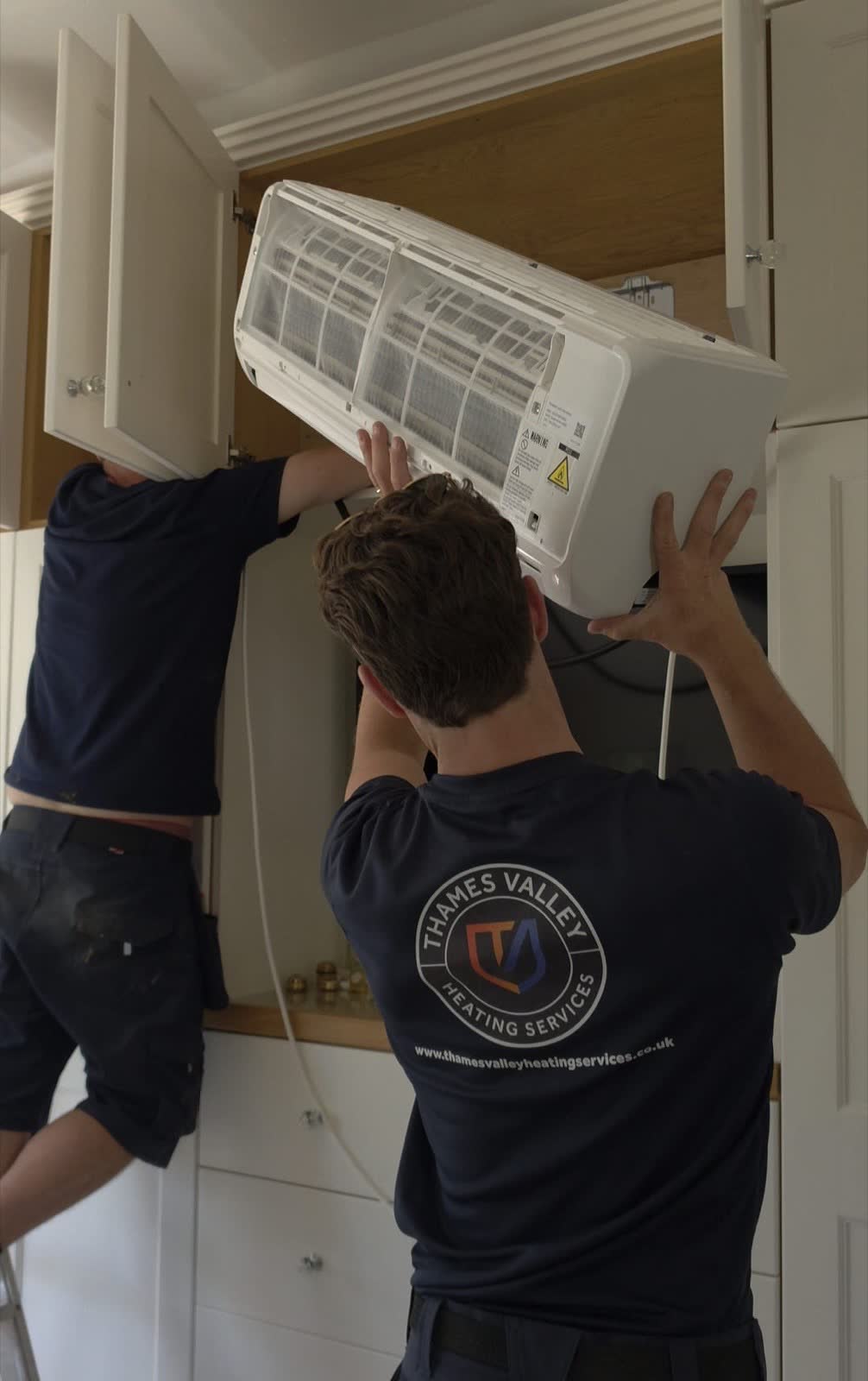 Two engineers lifting a wall mounted air conditioning unit into a bedroom cupboard during an installation in Eversley, Hampshire
