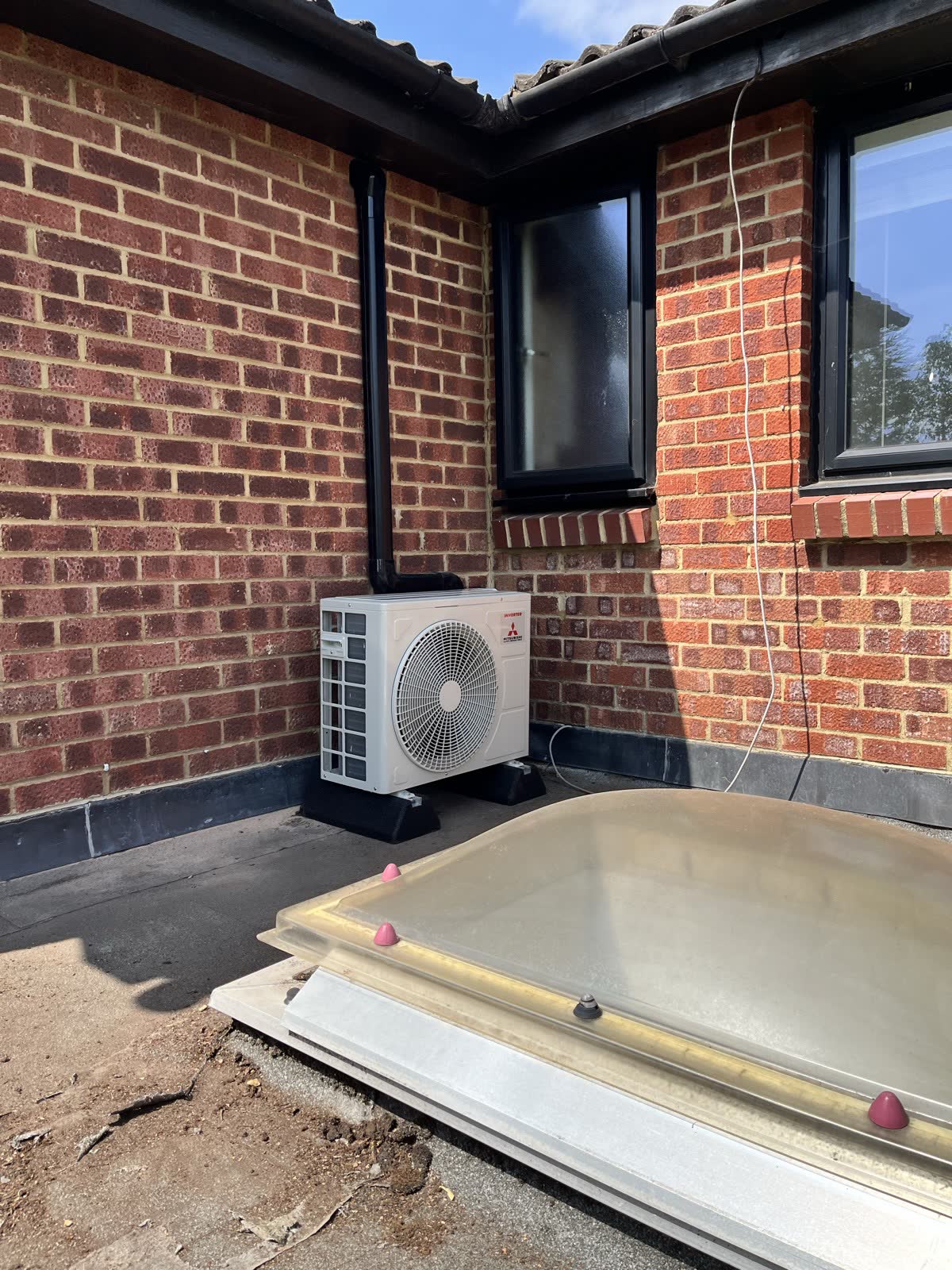 Outdoor air conditioning unit with black trunking run to match the existing downpipe and guttering