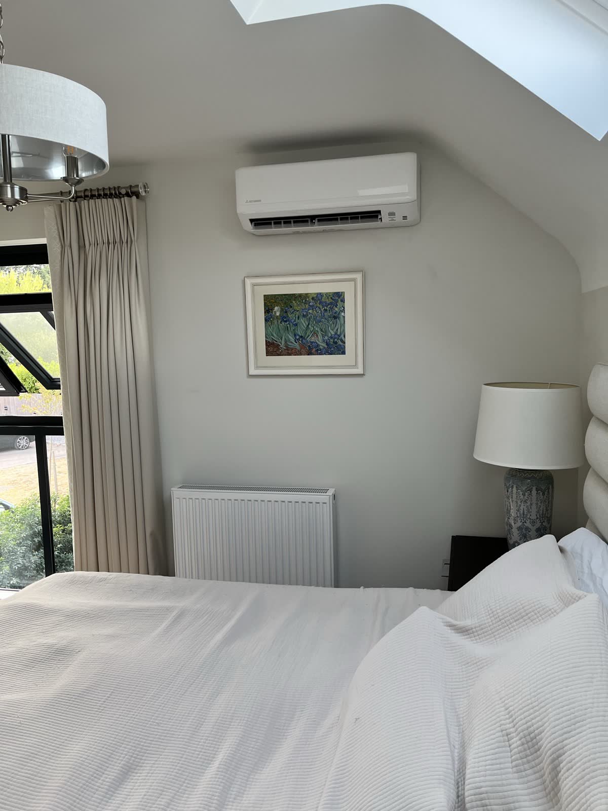 Wall mounted air conditioning unit installed high on a bedroom wall beneath a sloped ceiling