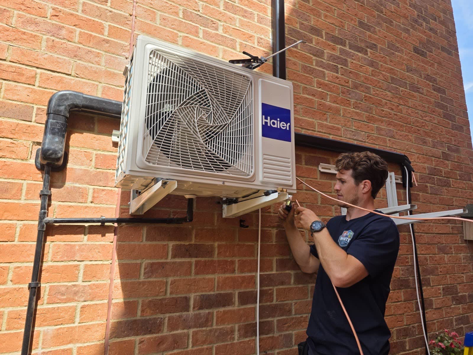 Engineer connecting pipework to a wall mounted Haier outdoor air conditioning unit