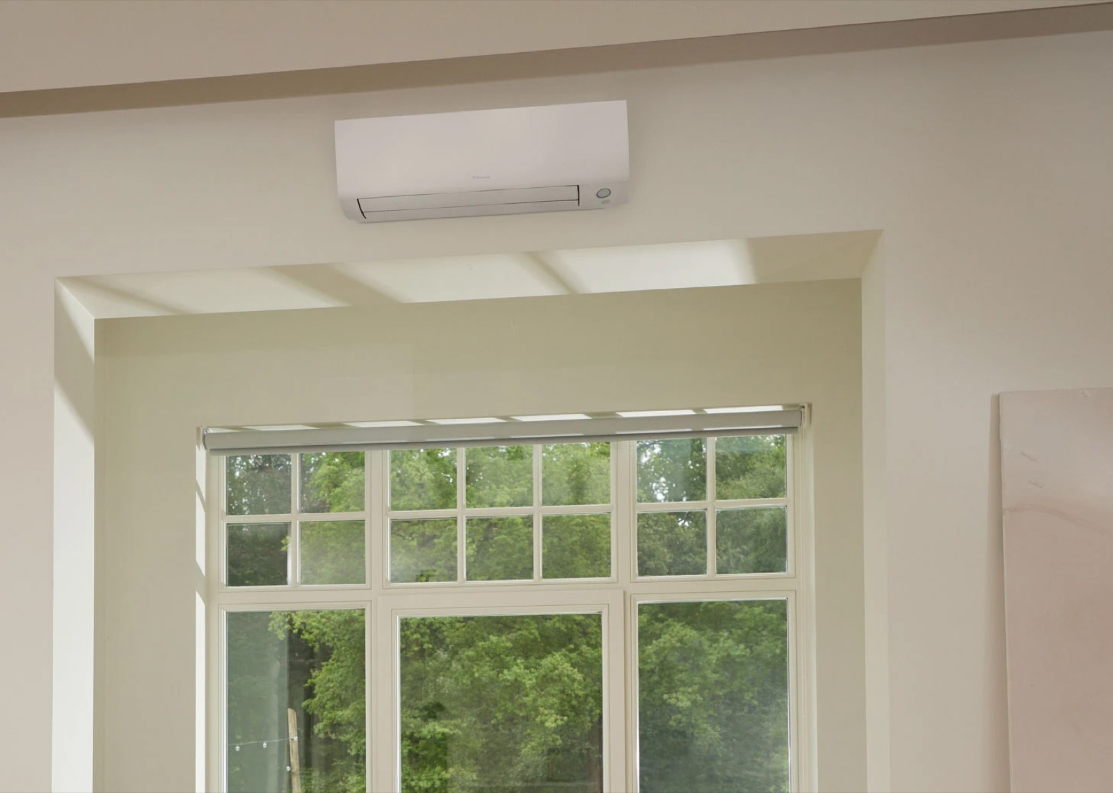 A wall mounted air conditioning unit installed above a window in a bright living room