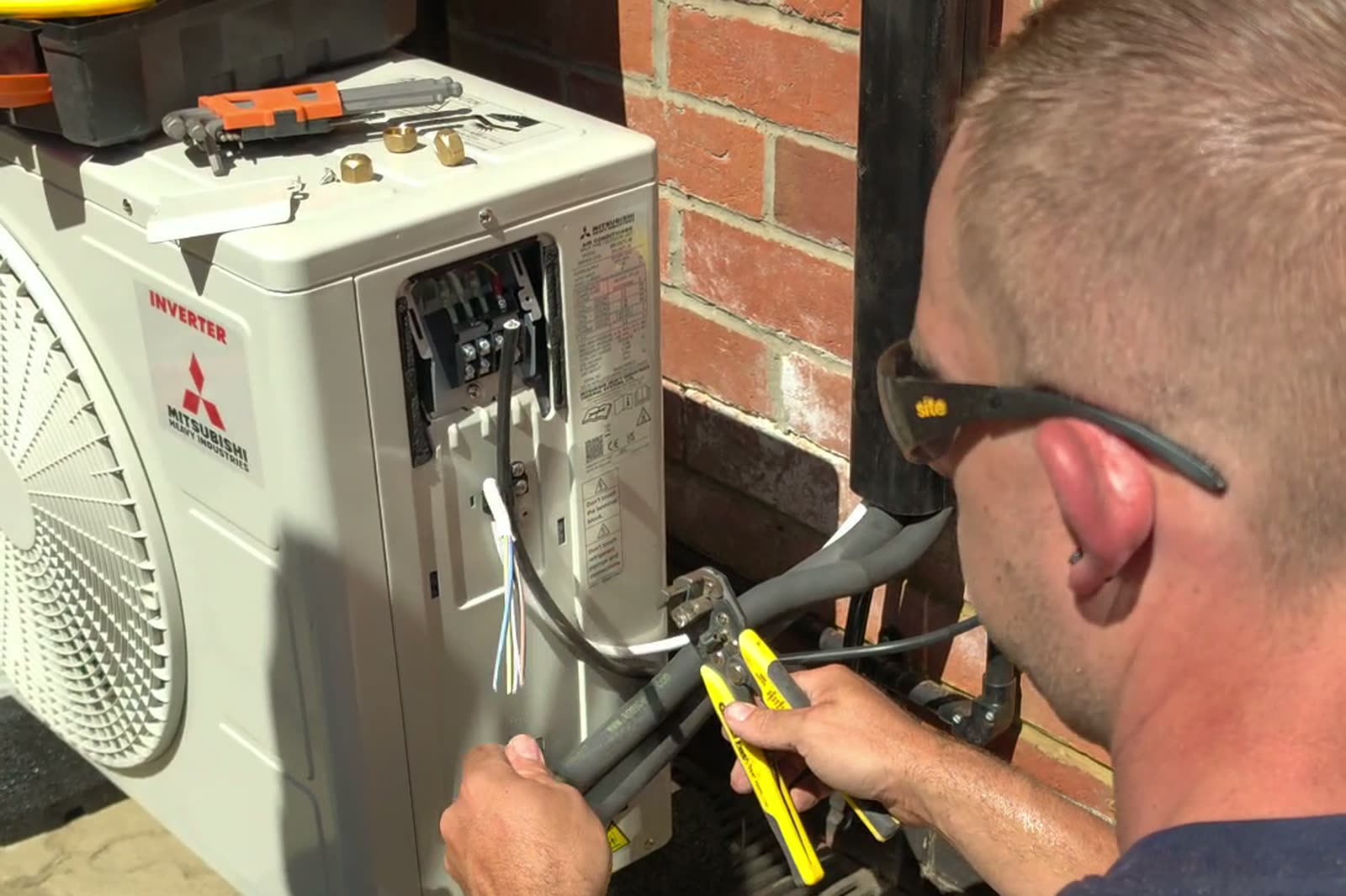 An engineer connecting the pipework and wiring at an outdoor air conditioning unit